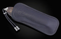 Folding knife with dark wooden handle partially visible in a dark textured leather sheath featuring an embossed logo and braided cord.