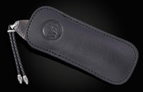 Folding knife with a patterned Damascus steel blade partially in a black leather sheath featuring an embossed logo and a braided lanyard.