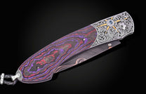 Luxury folding knife with purple-red marbled handle and engraved silver bolster by B12, featuring a blue gemstone and textured blade, side view on black background