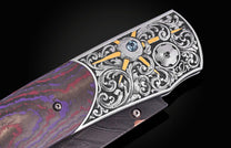 Luxury folding knife with purple and red damascus handle, ornate silver filigree, blue gemstone, and gold accents, side view
