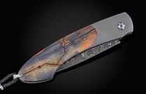 Folding knife with decorative blade and mammoth tooth handle on a black background