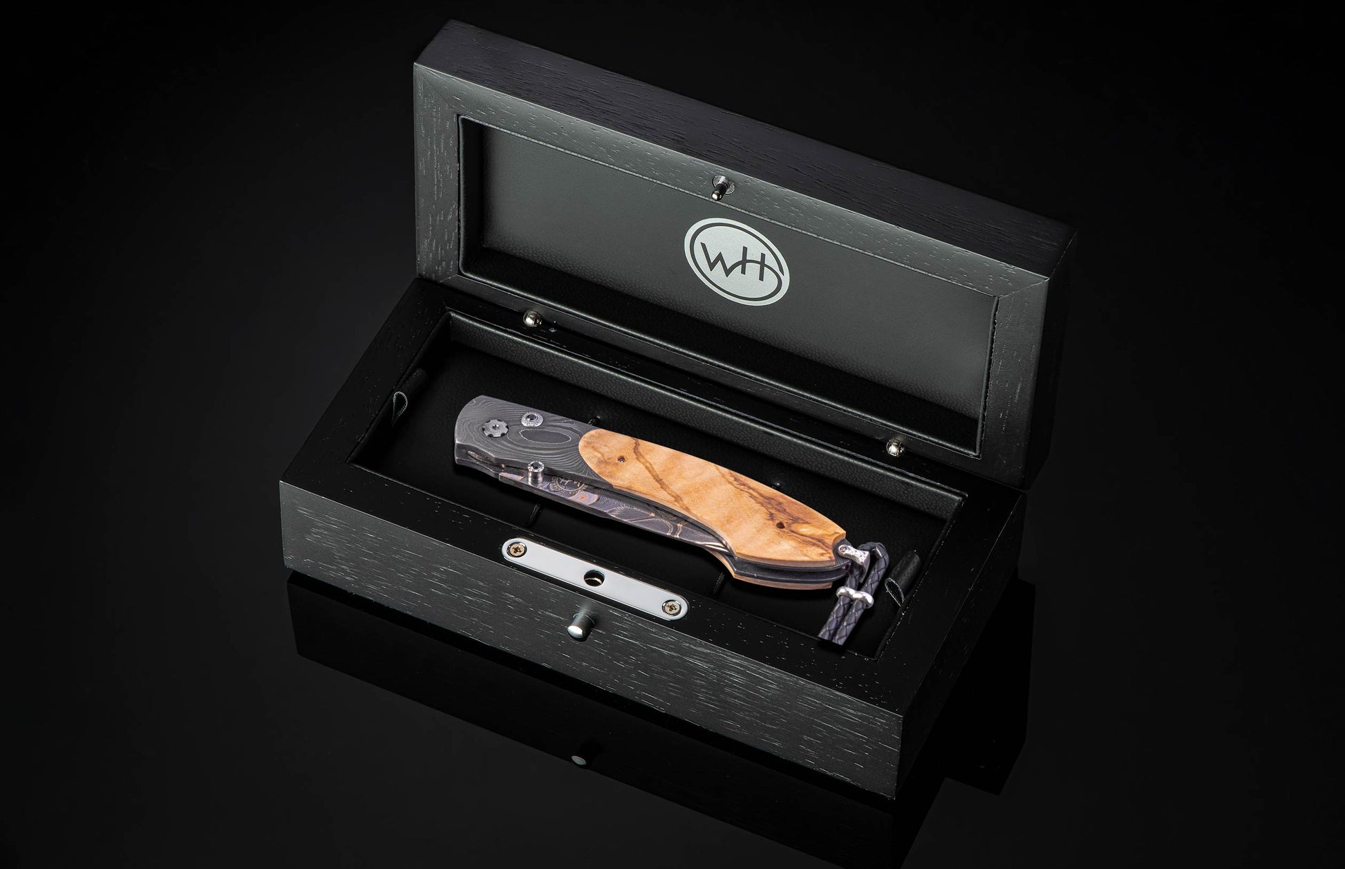 Black open box containing a William Henry knife on a black background