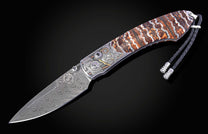 Folding knife with a wavy Damascus blade, ornate engraved bolster, striped stone handle, and black braided leather lanyard.