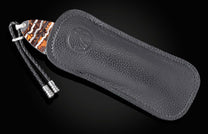 B12 Pirates knife, partially sheathed in dark gray pebbled leather with an embossed logo, featuring an abstract wavy handle and braided lanyard.