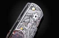 Engraved folding knife handle with a pirate skeleton, moon, and rope details, featuring a polished stone inlay.