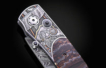 Folding knife handle featuring a detailed pirate engraving with gold accents, black gems, and a brown patterned stone inlay.
