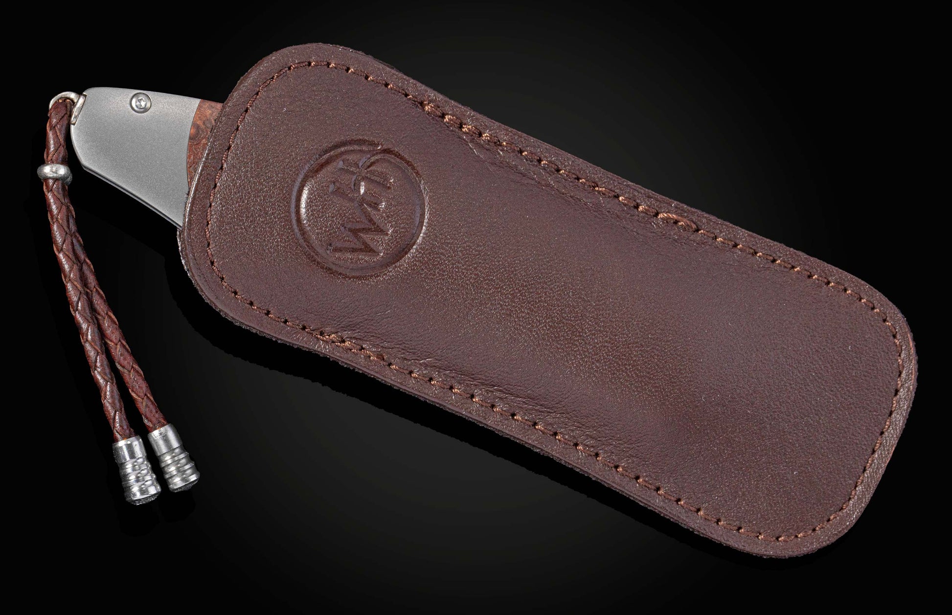 Knife with a metal end and dark handle, partially inserted into a brown leather sheath with an embossed logo, featuring a braided lanyard with metal tips.