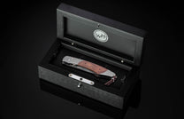 Folding knife with reddish-brown burl wood handle and silver-toned metal, displayed in an open black box with a 'WH' logo.