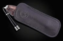 Red marbled handle knife with a black braided lanyard, partially inserted into a dark textured leather sheath with an embossed logo.