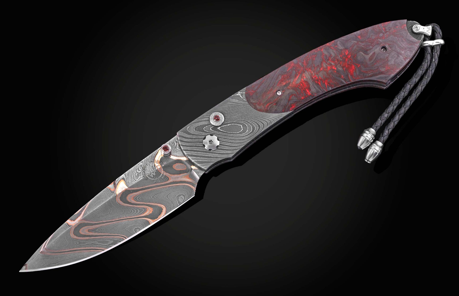 Folding knife with a Damascus blade, a red and black marbled handle, red gemstone accents, and a braided black leather lanyard.
