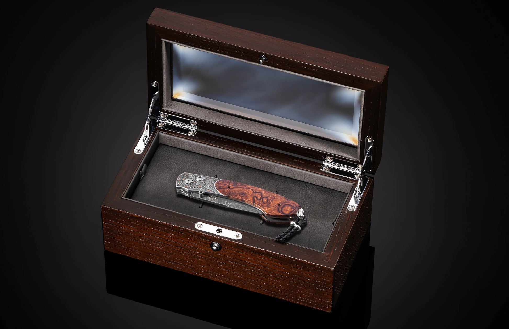 Folding knife with patterned blade and burl wood handle in wooden display case, side view, open lid, black interior, silver hardware