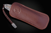 Decorative folding knife engraved with images from the Alamo on a black background