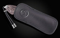 Western-style knife with patterned blade and black leather sheath by B12 WR, featuring embossed logo and braided lanyard, side view
