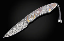 Damascus folding knife with an intricately engraved handle featuring watchmaker motifs and colored accents, and a black braided leather lanyard.