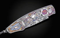 Ornate metal knife with intricate multi-colored skeleton and clockwork engraving, featuring a braided black leather lanyard.