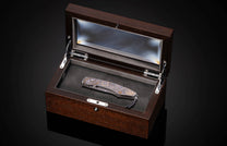 Intricately patterned knife with gold and blue accents, presented in an open dark wood display box.