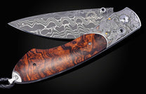 Folding knife with Damascus steel blade , hand engraving, and desert ironwood handle on a black background