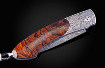 Folding knife with Damascus steel blade , hand engraving, and desert ironwood handle on a black background