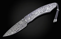 Damascus steel knife with an intricately engraved silver handle featuring "Route 66" and "100 Years" illustrations, blue gems, and a braided black leather lanyard.