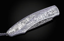 Metallic folding knife with detailed Route 66 landscape engraving, Damascus steel blade, and black braided lanyard.