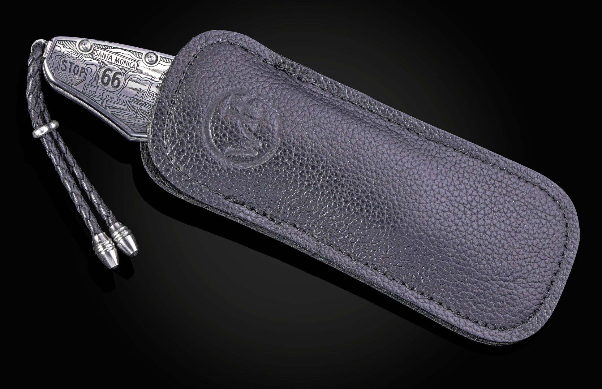 Engraved silver-tone knife with "Santa Monica", "Stop 66" and pier details, partially in a dark pebbled leather sheath with an embossed logo and braided lanyard.