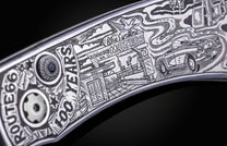Metal knife with detailed engraved artwork depicting a Route 66 scene, including a motel, vintage car, and "100 YEARS" text.