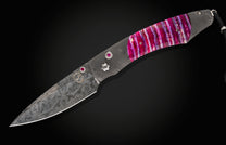 Damascus folding knife by B12 with vibrant pink stabilized wood handle and ruby inlays.