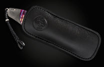 Folding knife with purple handle and damascus blade in embossed black leather sheath, shown on dark background.