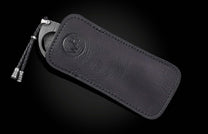 Black leather cigar cutter with damascus steel blade and braided cord, by CG1 Heirloom, featuring embossed logo and precise stitching, side view on dark background