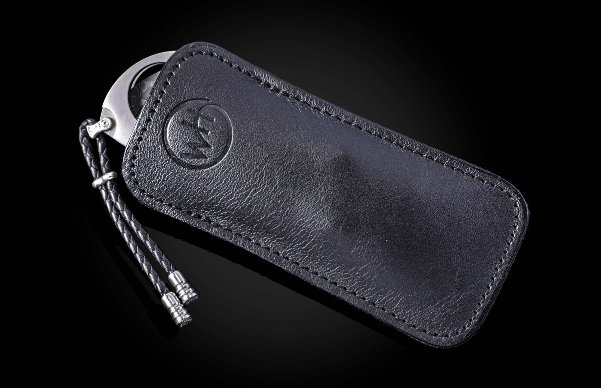 Black leather cigar cutter with silver blade and braided cord, by CG1 Kingman, featuring embossed logo and precise stitching, side view on dark background