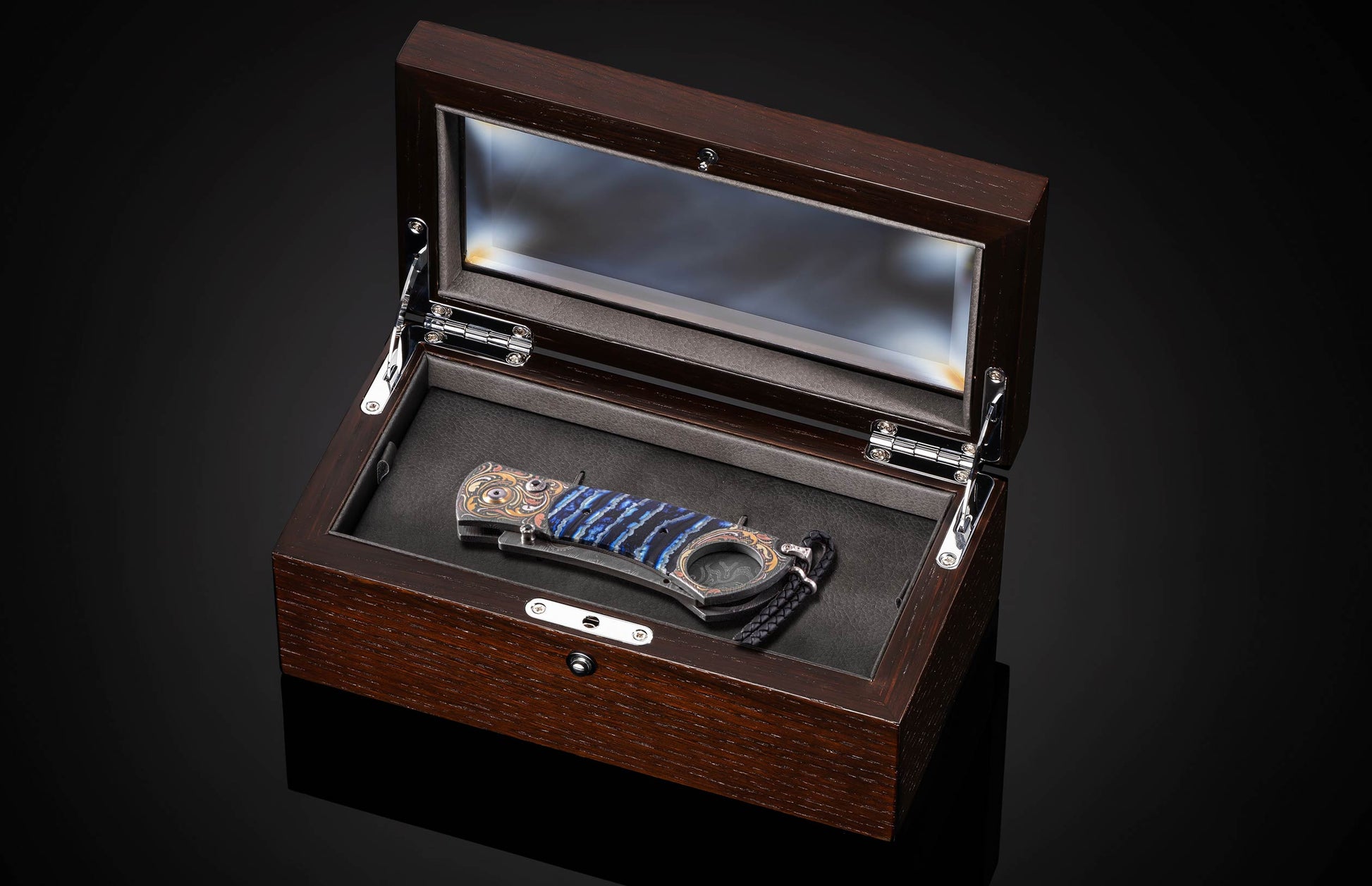 Luxury cigar cutter with blue striped handle and ornate metal accents, displayed in dark wood presentation box with glass lid.