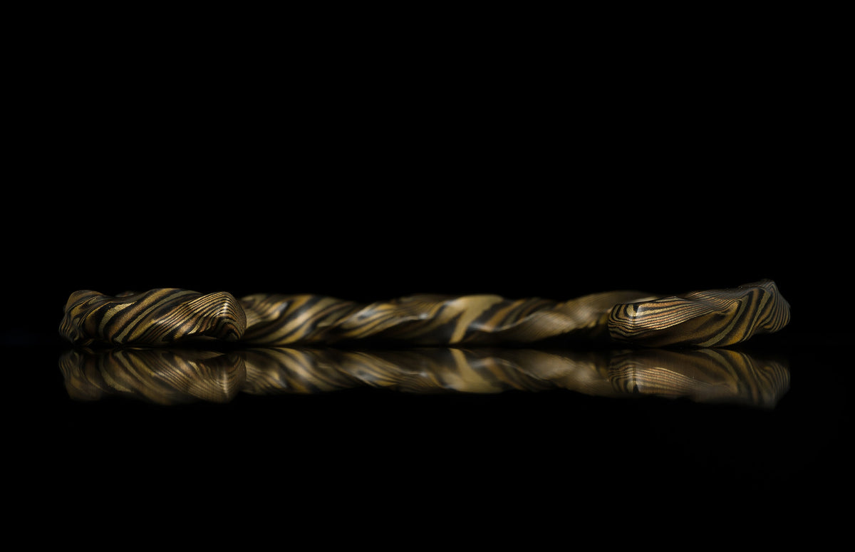 Twisted gold and black layered ring with marbled texture, side view on reflective surface