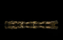 Twisted gold and black layered ring with marbled texture, side view on reflective surface