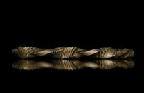 Twisted gold and dark metal mokume-gane ring with flowing striped pattern, side view on reflective black surface