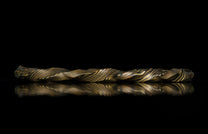Twisted gold and dark patterned bracelet by HC13 RIFTBORN, showcasing intricate marbled texture with reflective surface, side view on black background