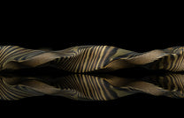 Twisted gold and black damascus steel ring by HC13 RIFTBORN, showcasing intricate layered pattern with reflective surface, side view on dark background