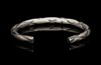 Silver bracelet with a textured design on a black background