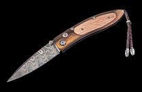 Decorative folding knife with a wavy Damascus blade, brown wood handle with a lighter inlay, yellow gemstone accents, and a braided leather lanyard.