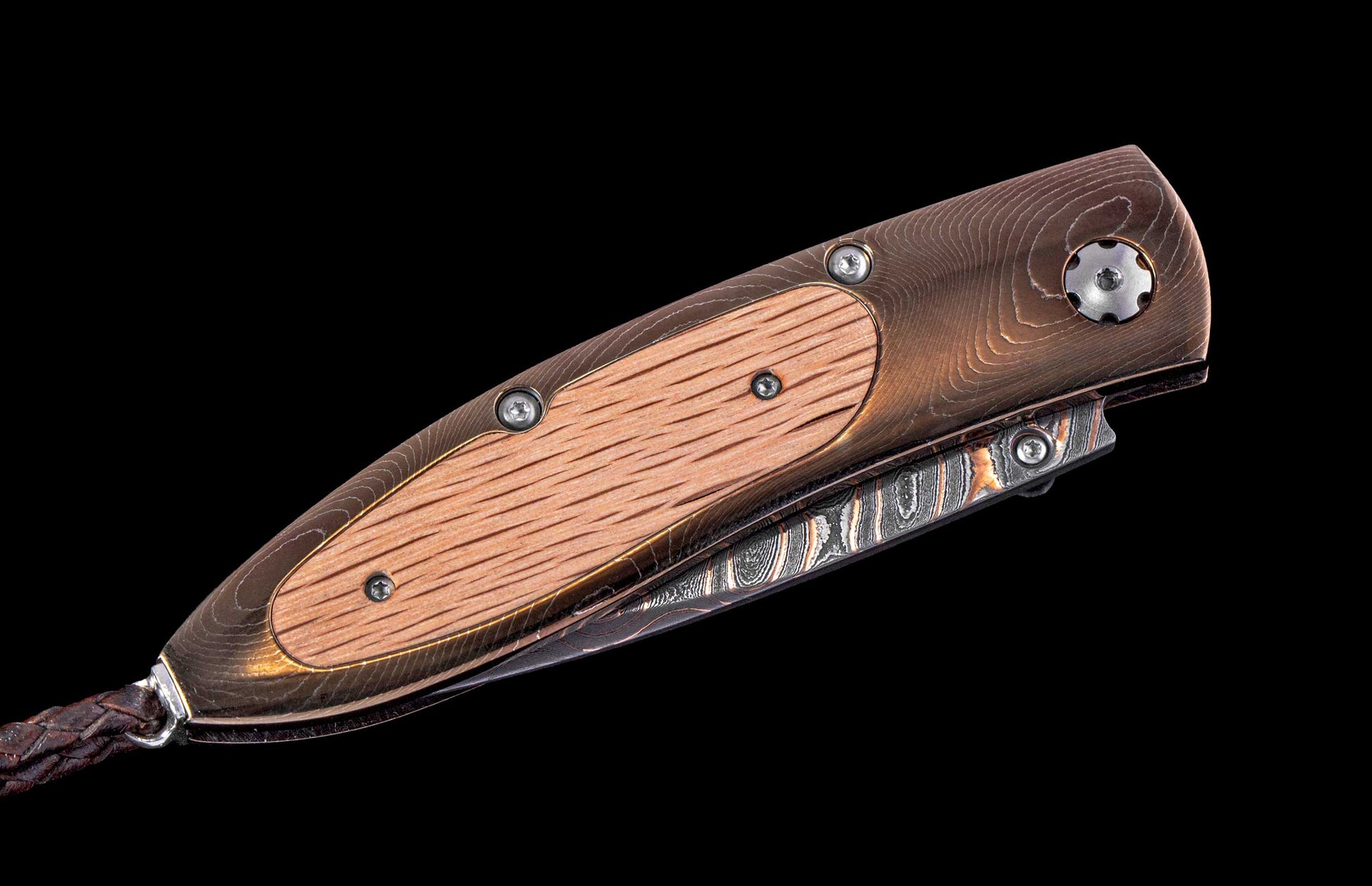 Folding knife with bronze-toned handle, light wood inlay, Damascus steel blade, and braided leather lanyard.