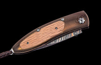 Folding knife with bronze-toned handle, light wood inlay, Damascus steel blade, and braided leather lanyard.
