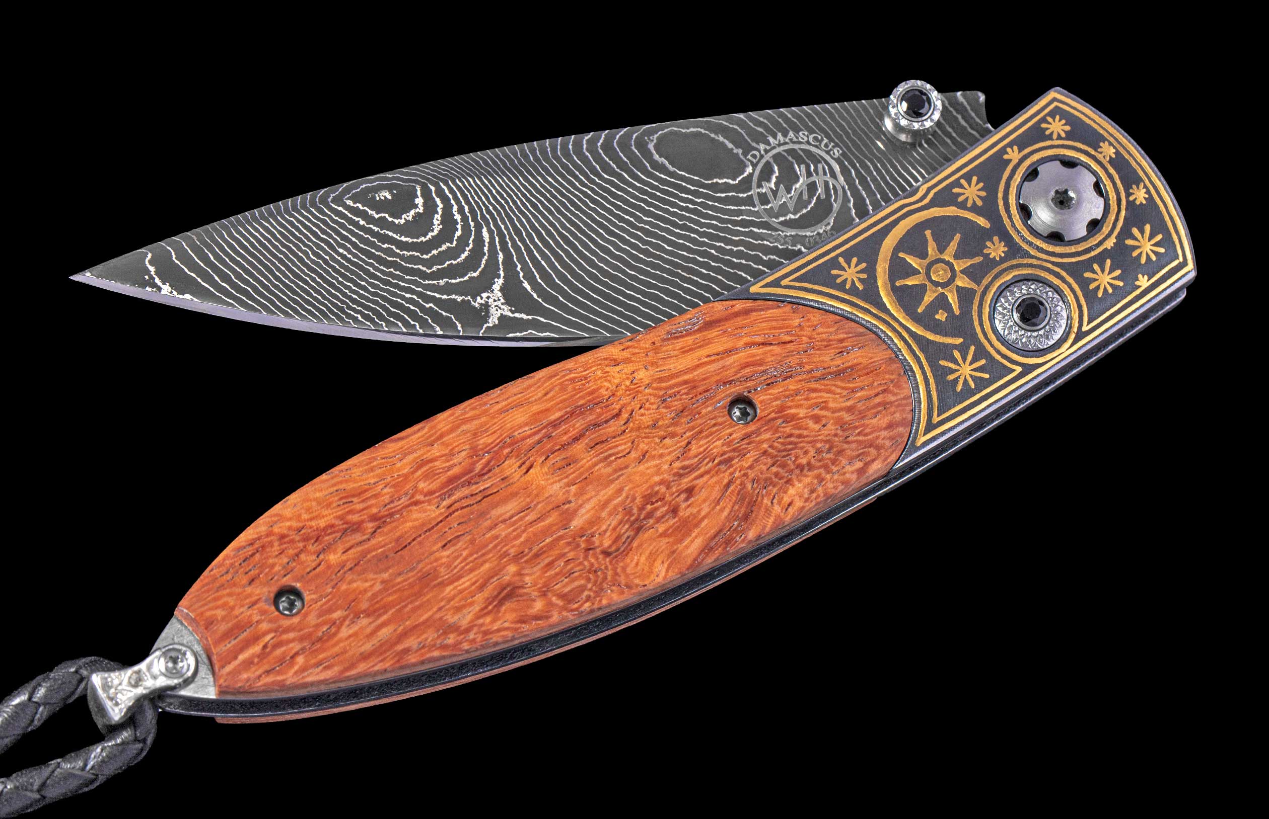 Open folding knife with Damascus steel blade marked 'DAMASCUS', orange wood handle, engraved dark metal with gold patterns, and a black braided lanyard.