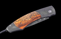 Folding knife with a rich brown wood handle, Damascus patterned metal, and a black braided leather lanyard.