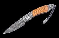 An open folding knife with a patterned Damascus steel blade, a light brown wooden handle, and detailed silver-colored metal featuring an eagle and stars, with a braided leather lanyard.