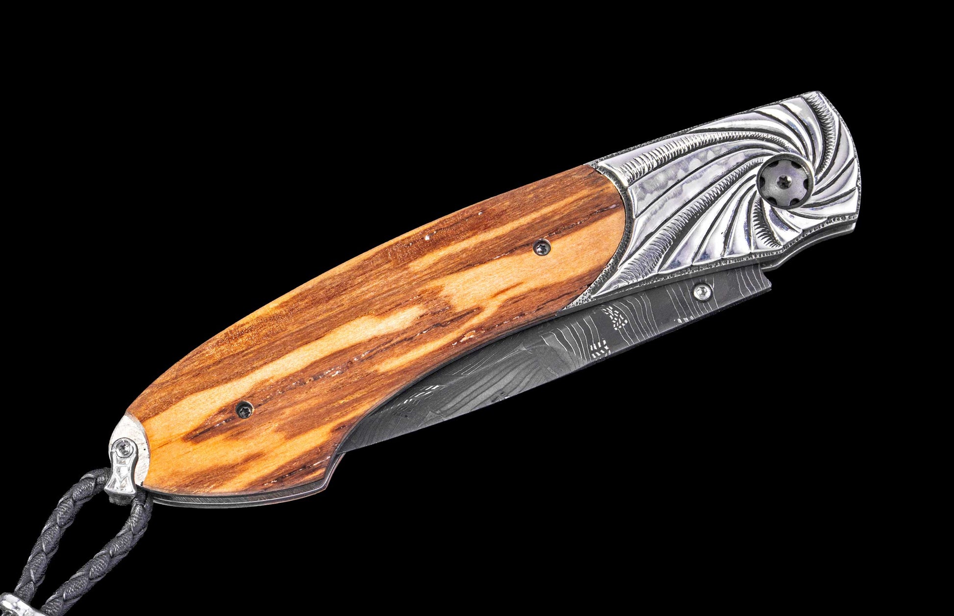 Folding knife with a striped light brown wood handle, ornate silver metal with swirling engravings, a Damascus steel blade, and a black braided lanyard.