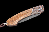 Foldable knife with wooden handle and patterned blade on a black background