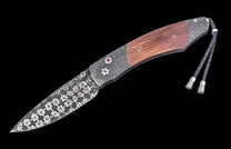 Ornate folding knife with a brown wooden handle, Damascus steel blade with floral etching, red gemstones, and a braided leather lanyard.