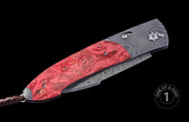 Red burl wood handle folding knife with Damascus steel frame, braided leather cord, and 'ONE OF A KIND 1' label.