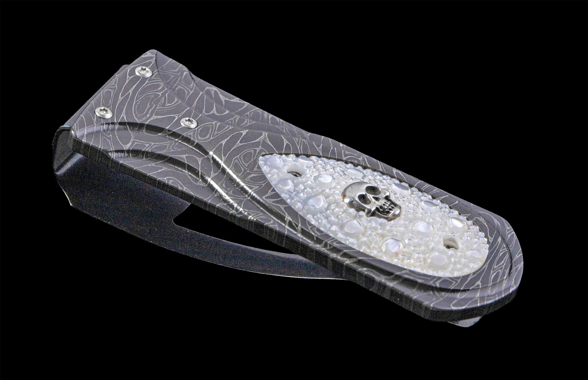 Money Clip with damascus steel frame and a silver skull set in carved mother of pearl on a black background