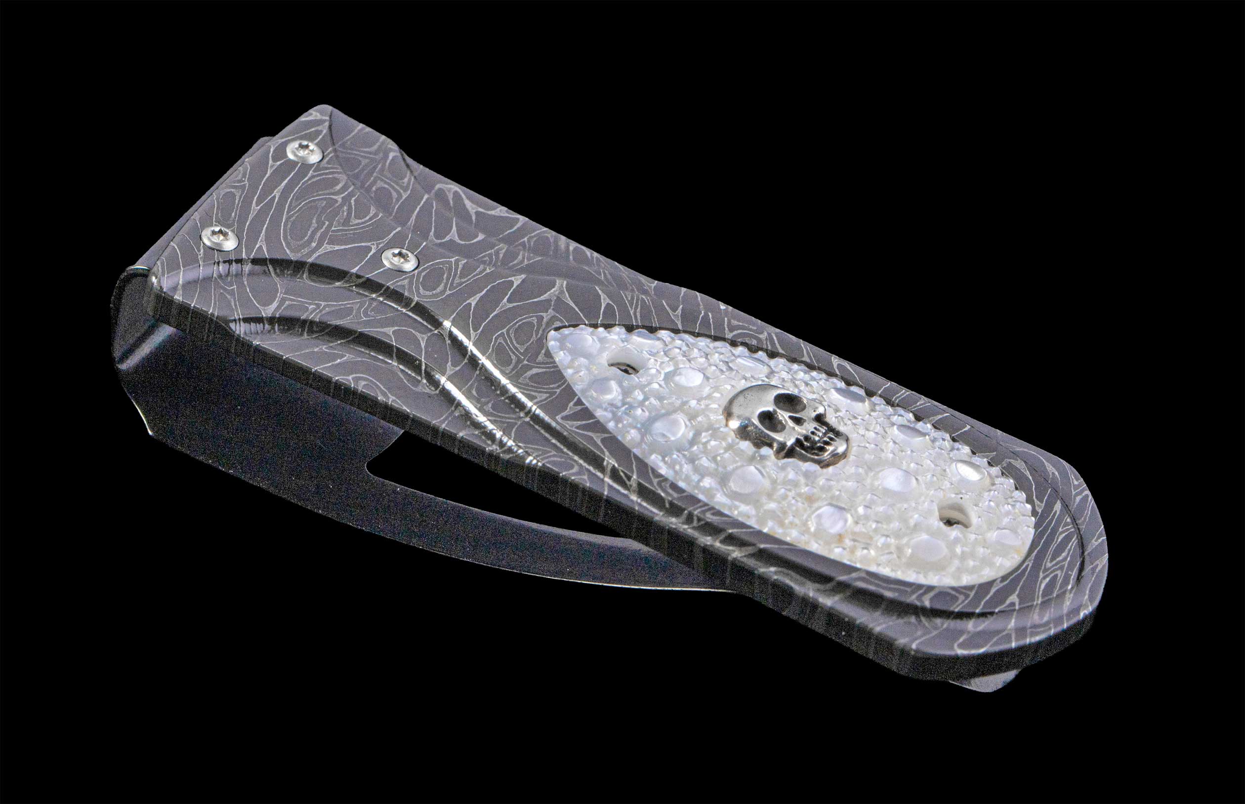 Money Clip with damascus steel frame and a silver skull set in carved mother of pearl on a black background