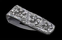 Silver metal money clip with an engraved skull, intricate scrollwork, and textured background, viewed at an angle.